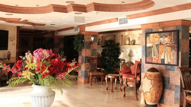 A lobby with a large white vase of flowers, wooden furniture, and a large painting on the wall. - Gulf Park Hotel Apartment (Dammam)