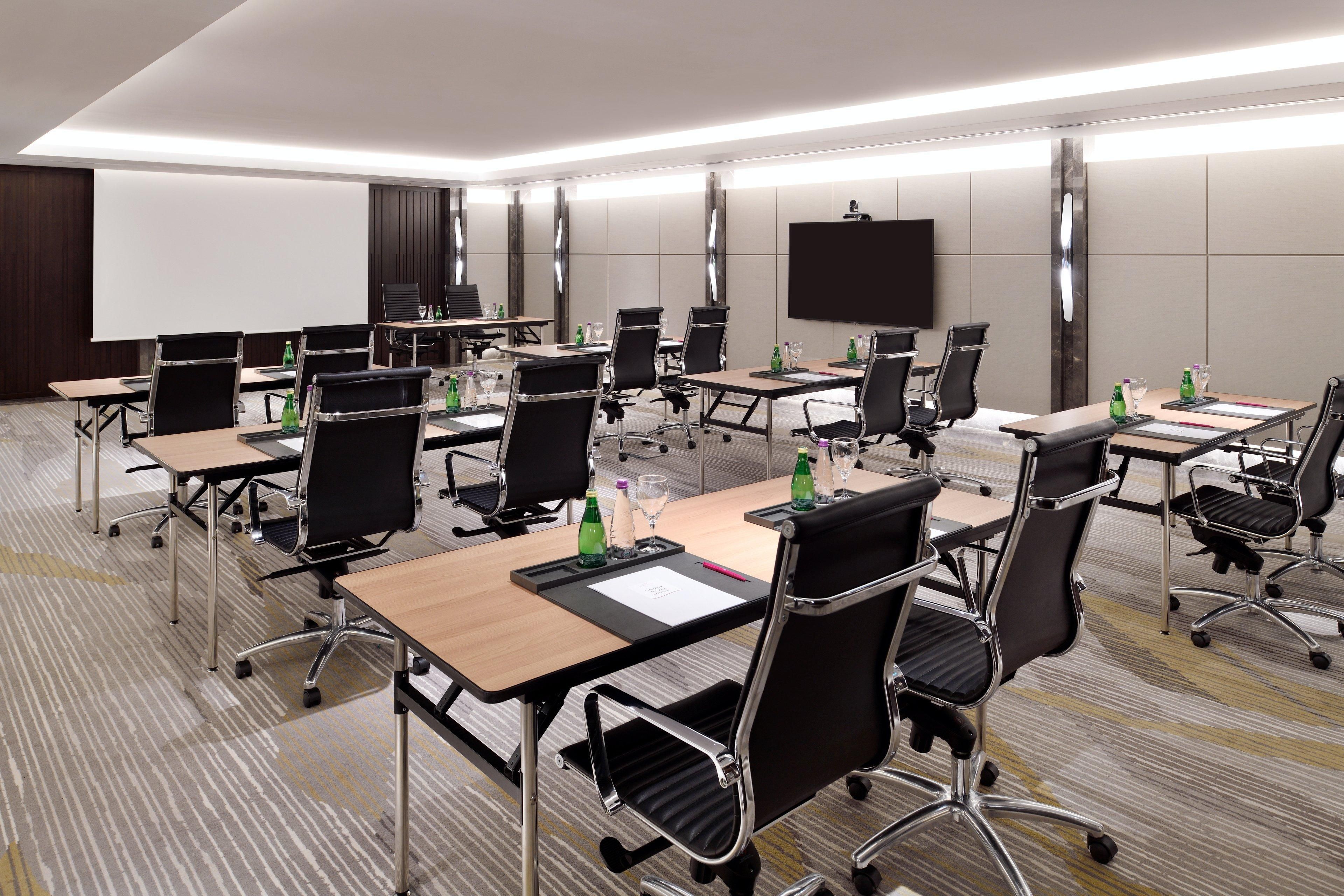 Un salón de conferencias con varias mesas, sillas y una pantalla grande.