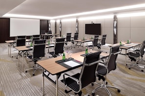 A conference room with multiple tables, chairs, and a large screen.