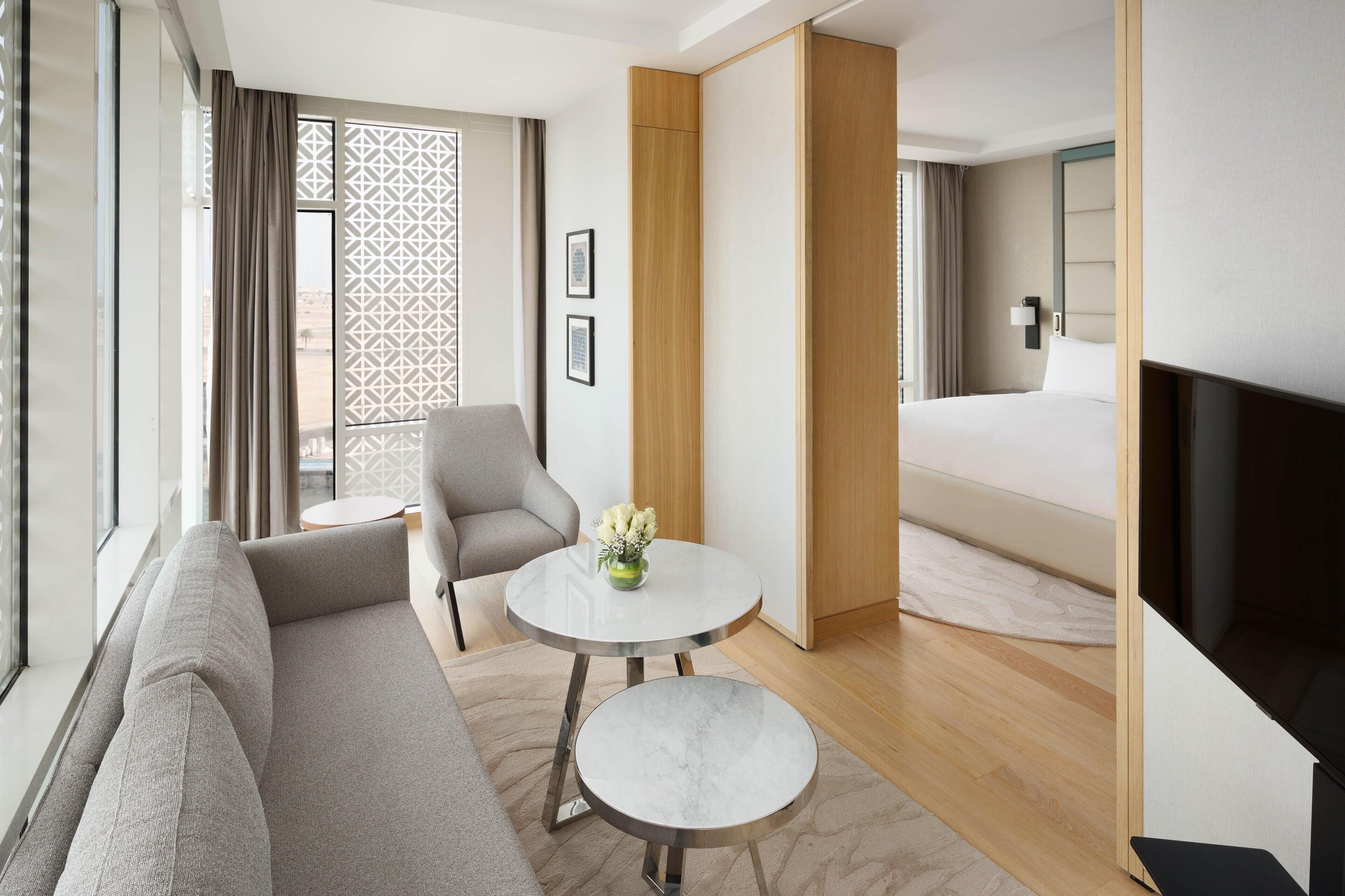 Une chambre d’hôtel moderne avec un canapé, une petite table ronde ornée d’un vase, un lit et un téléviseur.