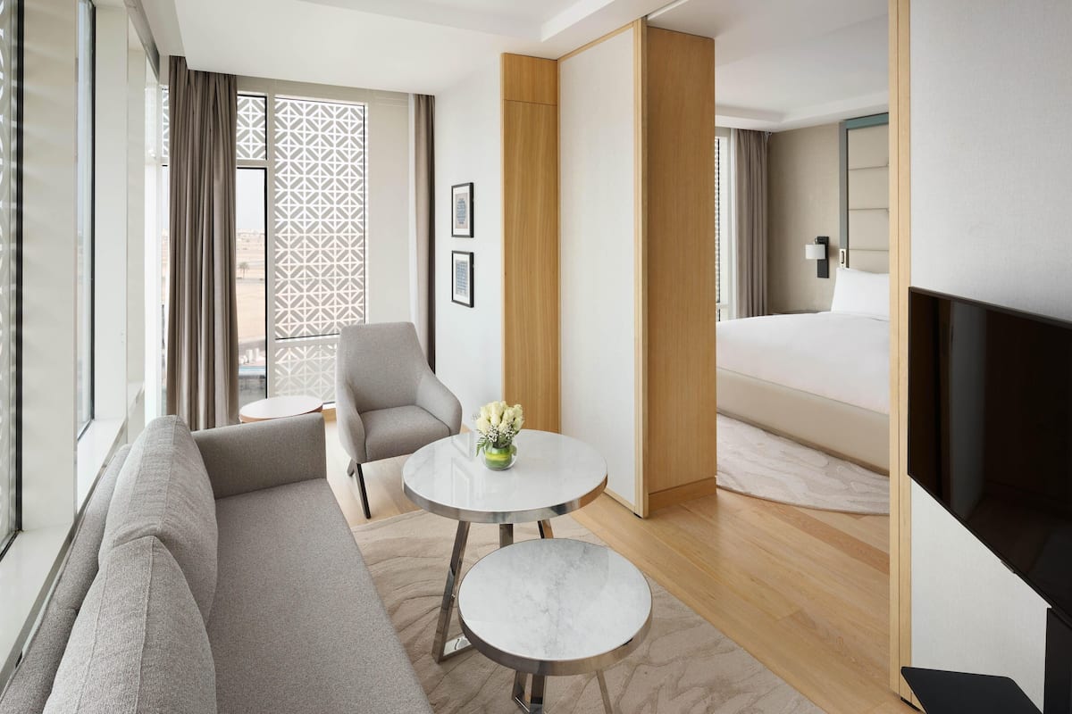 Ein modernes Hotelzimmer mit Sofa, einem kleinen runden Tisch mit Vase, einem Bett und einem Fernseher.