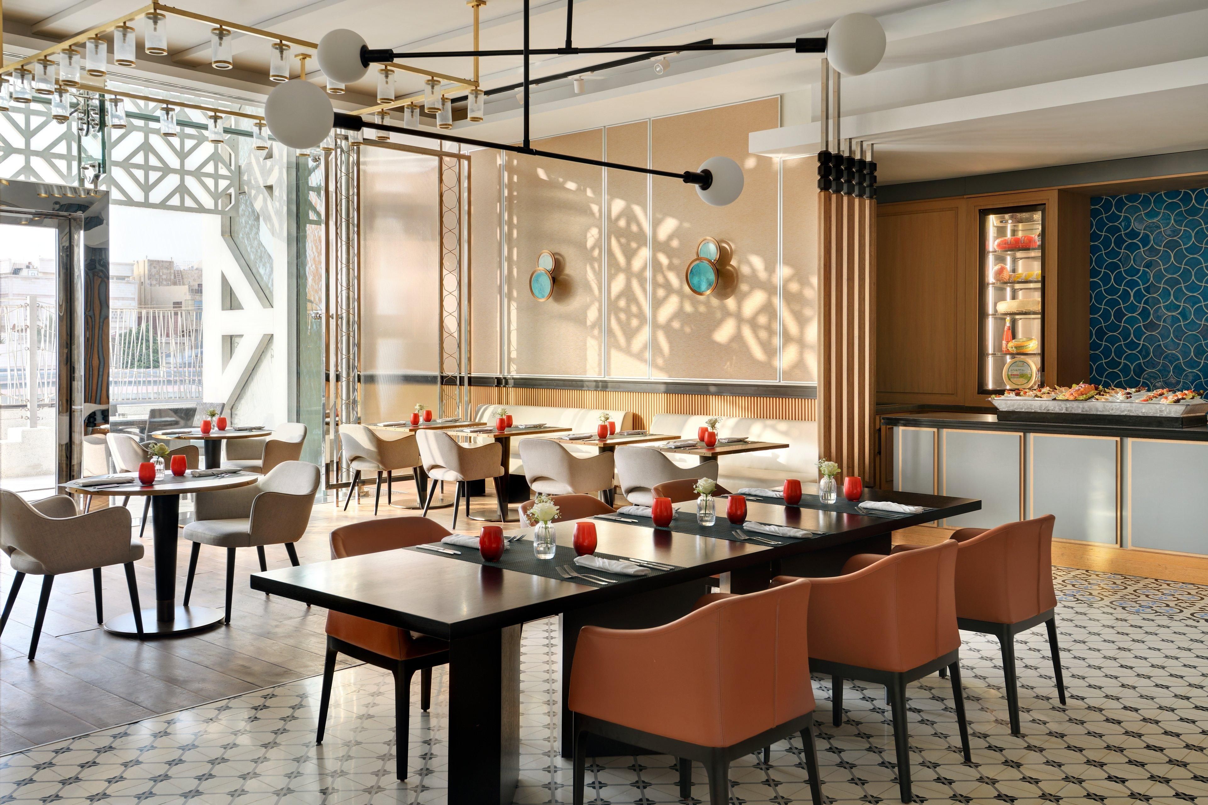 Un restaurante moderno con mesas redondas, sillas anaranjadas y una pared decorativa con patrones geométricos.