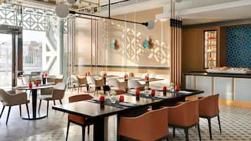 Un restaurante moderno con mesas redondas, sillas anaranjadas y una pared decorativa con patrones geométricos.