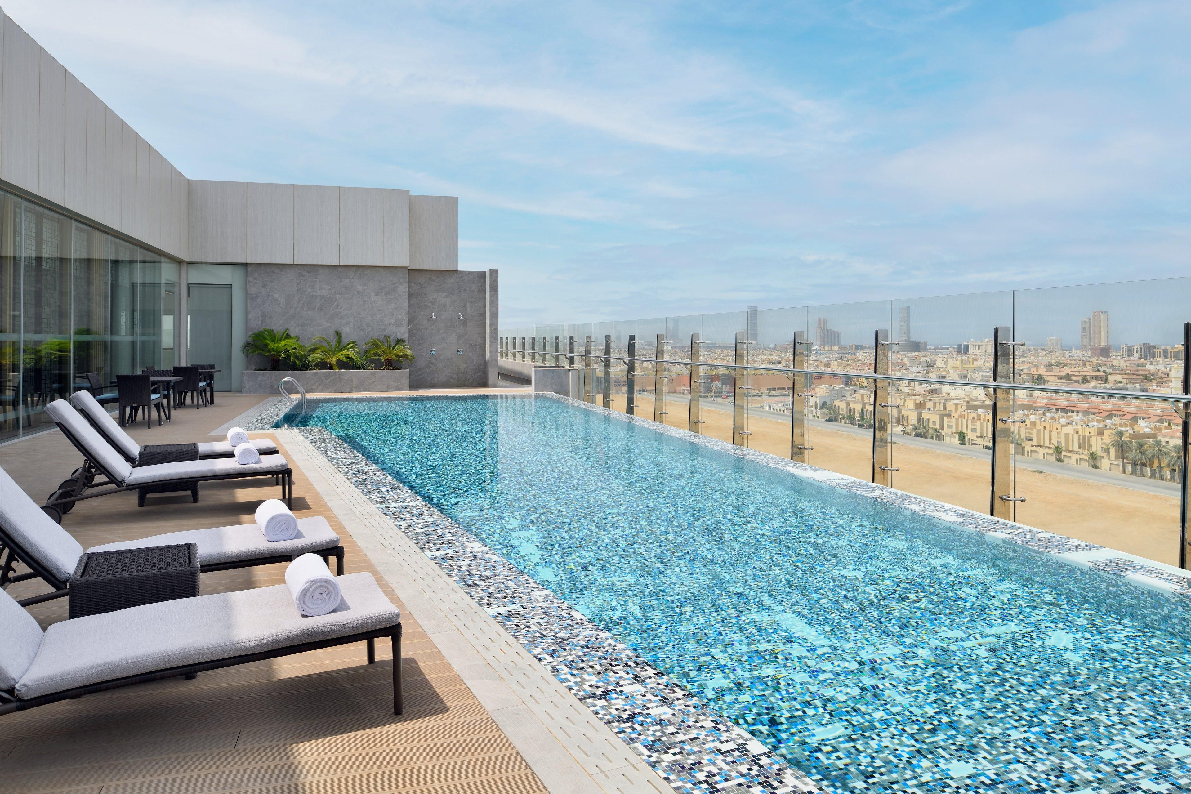 Piscina infinita en la azotea con sillones de descanso, barandilla de vidrio y vistas a la ciudad.