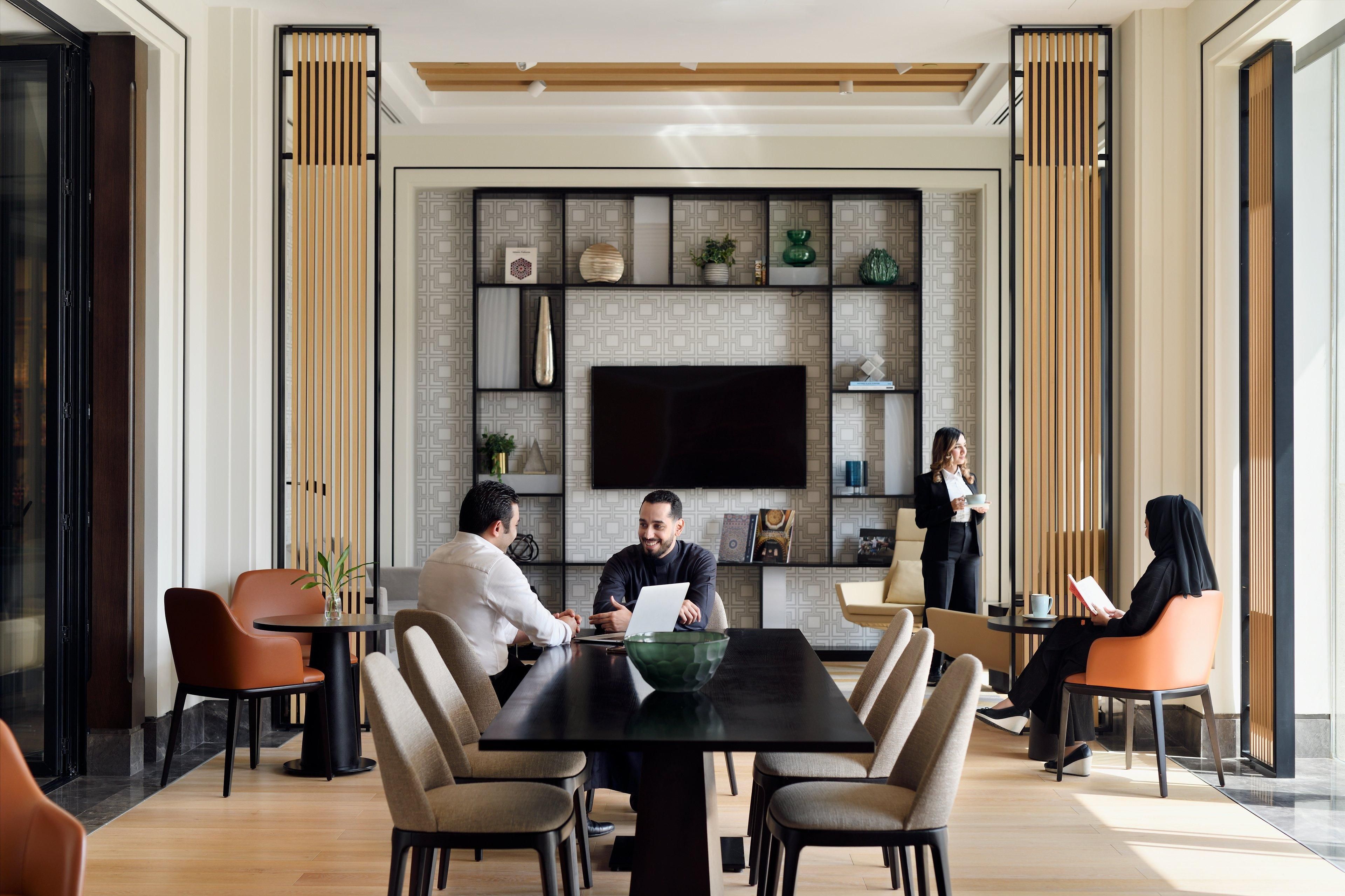 Una sala de reuniones moderna con una gran mesa, sillas, un televisor y estanterías decorativas.
