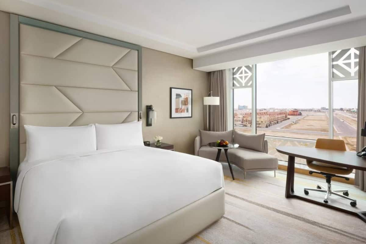 Ein Hotelzimmer mit einem großen Bett, einem Schreibtisch, einem Stuhl und Blick auf eine Baustelle.