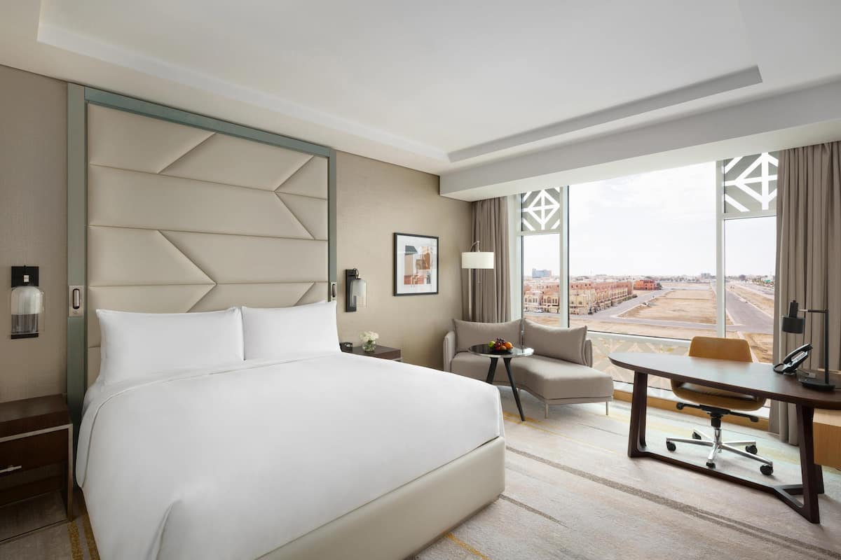 Ein Hotelzimmer mit einem großen Bett, einem Schreibtisch, einem Sessel und einer Sitzecke, mit Blick auf die Stadt.