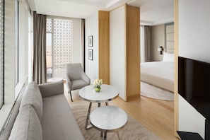 Una habitación de hotel moderna con un sofá, una mesita redonda con un jarrón, una cama y un televisor.