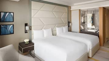 A hotel room with two beds, a nightstand, a chair, a wall-mounted lamp, and a mirror.