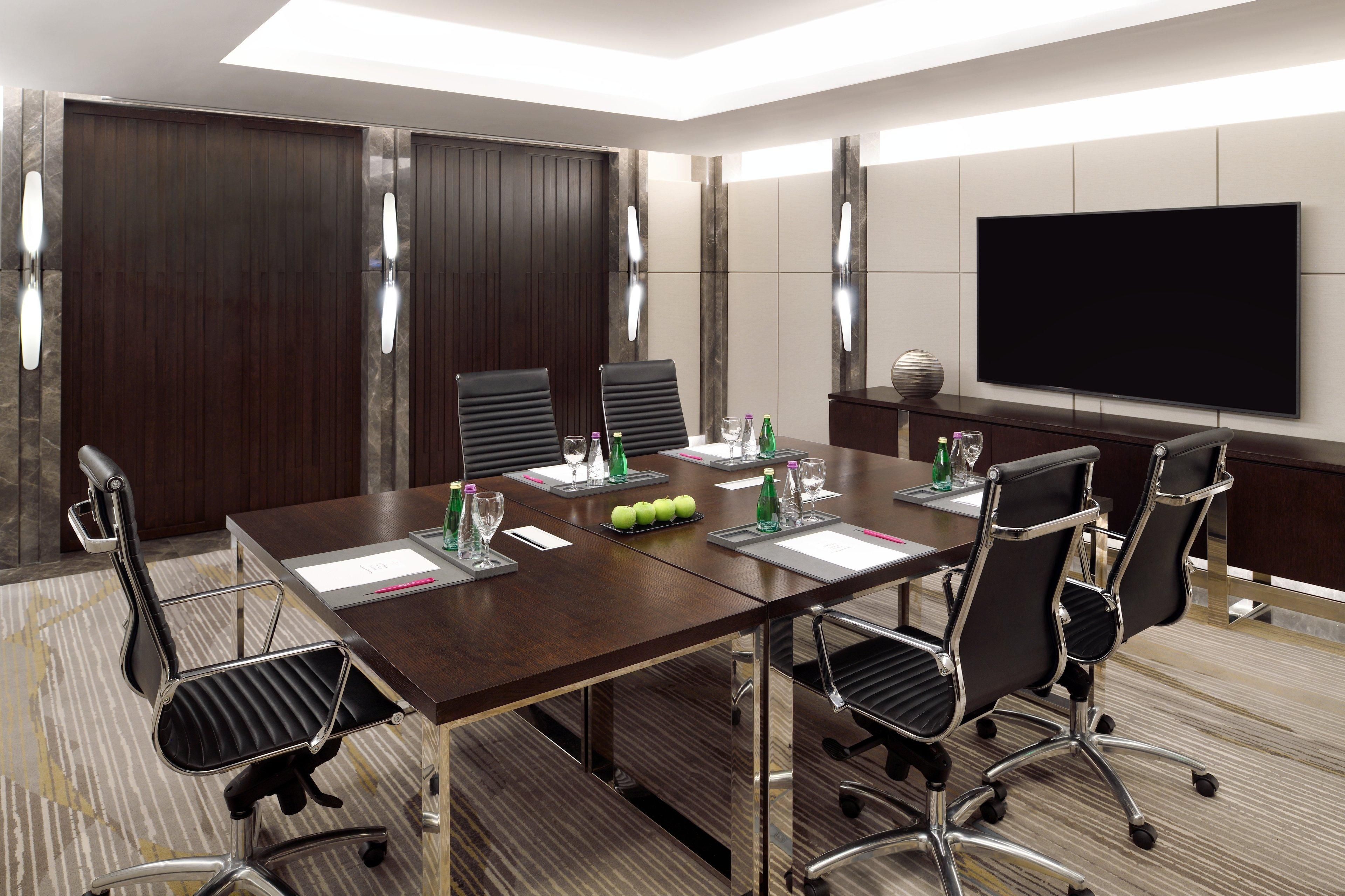 A conference room with a long table, six chairs, a flat-screen TV, and a wooden partition wall.