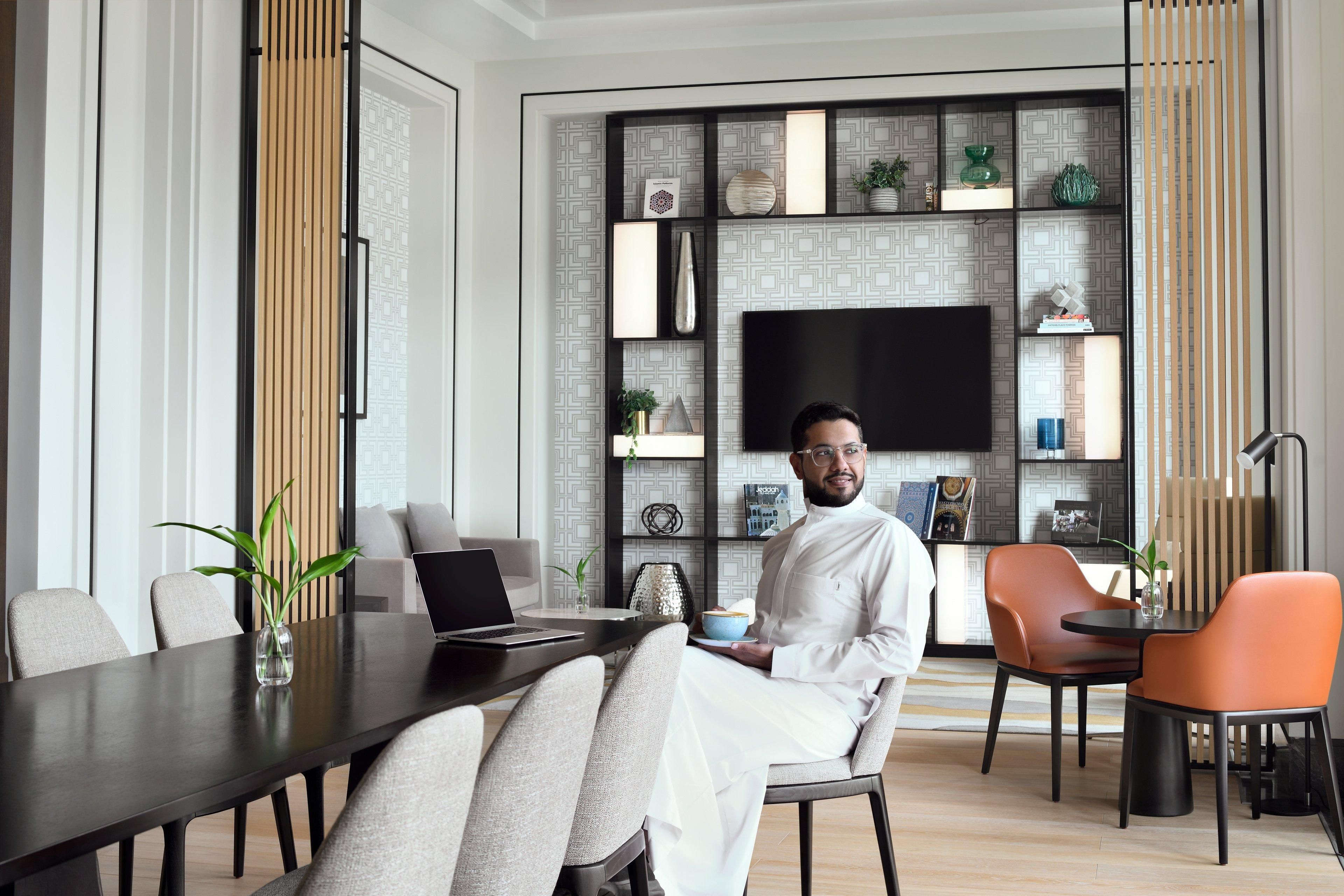 A modern interior with a dining table, chairs, a laptop, a TV, and decorative items on shelves.
