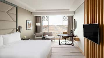 Habitación de hotel con una cama grande, un escritorio, una silla, un televisor y vistas al aeropuerto.