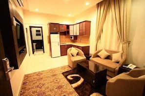 A compact living space with a kitchenette, a sofa set, and a patterned rug. - Rest Night Serviced Apartments - AL Nafal (Riyadh)