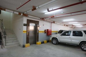 A parking garage with a white SUV parked near a staircase and a fire extinguisher mounted on the wall. - Rest Night Serviced Apartments - AL Nafal (Riyadh)