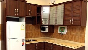 A compact kitchen with dark wooden cabinets, a white refrigerator, a microwave, and a gas stove. - Rest Night Serviced Apartments - AL Nafal (Riyadh)