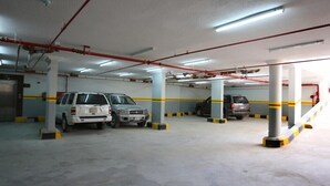 A multi-level parking garage with concrete pillars, fluorescent lighting, and yellow and black striped barriers. - Rest Night Serviced Apartments - AL Nafal (Riyadh)