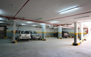 A multi-level parking garage with concrete pillars, fluorescent lighting, and yellow and black striped barriers. - Rest Night Serviced Apartments - AL Nafal (Riyadh)