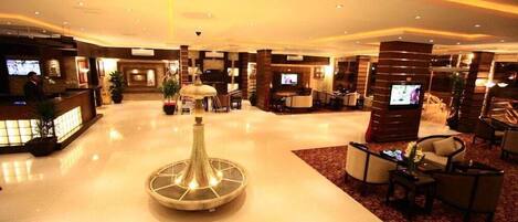 A spacious lobby with a central decorative fountain, multiple seating areas, and a reception desk with televisions.