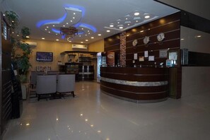 Zona de recepción de hotel con un mostrador curvo, un televisor montado en la pared y un candelabro.
