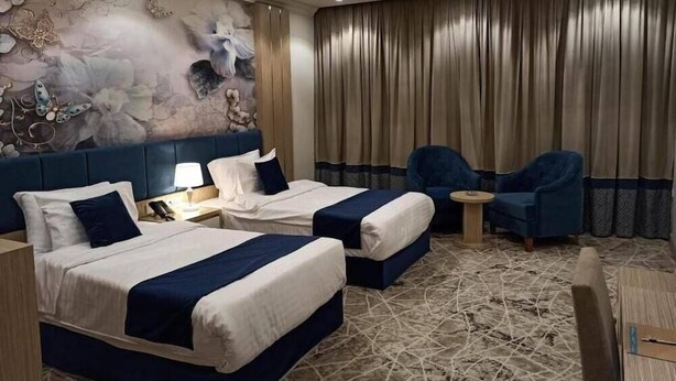 A hotel room with two beds, a large wall mural, a curtain, and two blue armchairs. - Reef Home Luxury Hotel (Riyadh)