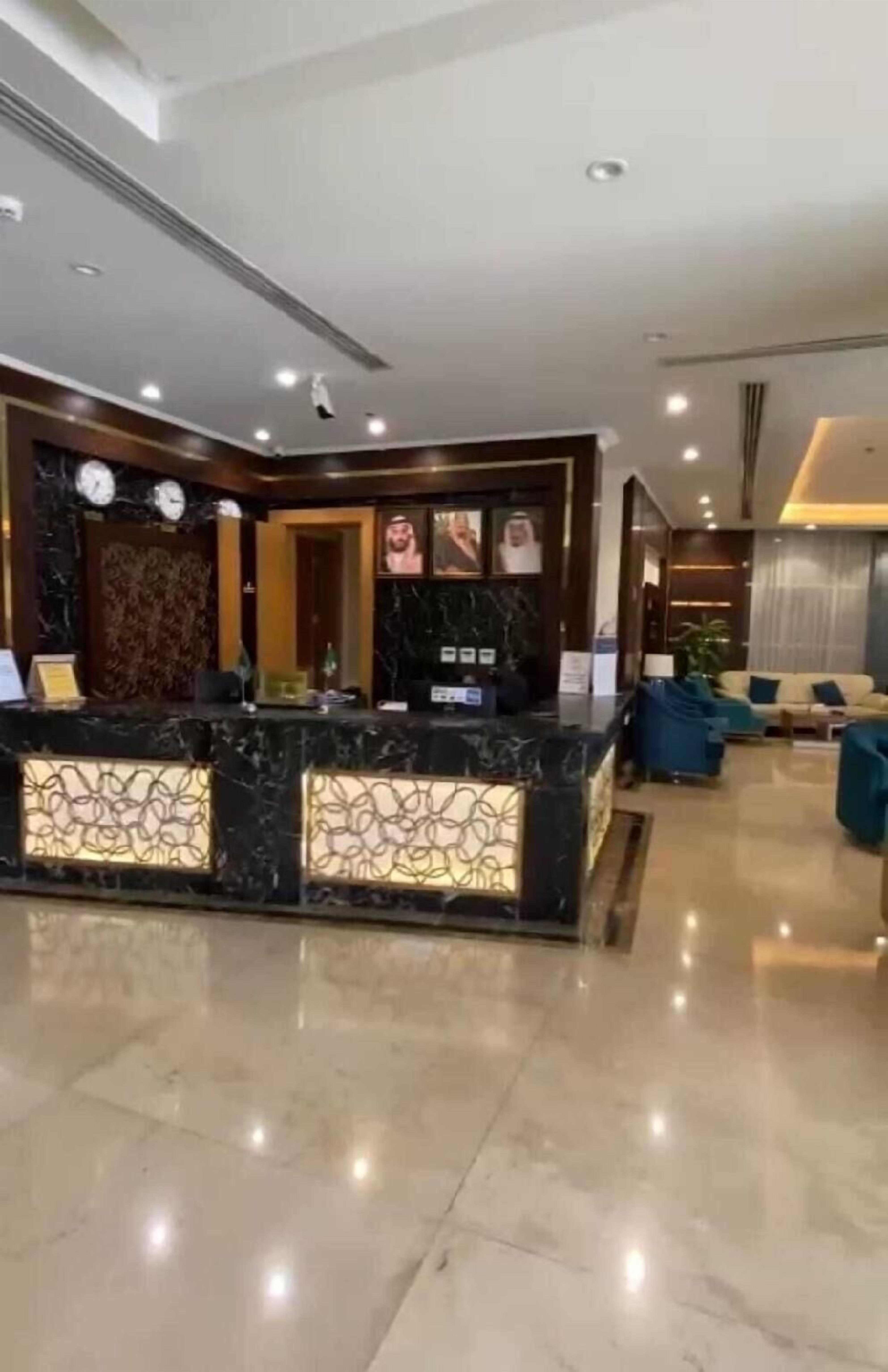 Zona de recepción de un hotel con un mostrador de mármol, un área de estar con sofás y un reloj en la pared.