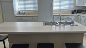 Eine Küche mit Kochinsel, drei schwarzen Barhocker, Deckenventilator und Kühlschrank.