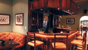A bar area with a wooden bar counter, cushioned seating, and framed artwork on the walls. - Pakamisa Private Game Reserve (Pongola)