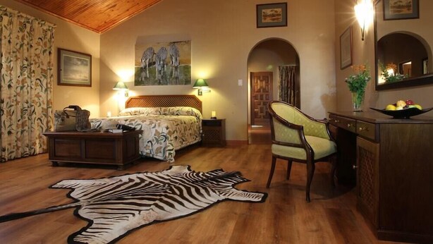 A bedroom with a bed, a chair, a desk, a zebra rug, and a painting of zebras. - Pakamisa Private Game Reserve (Pongola)