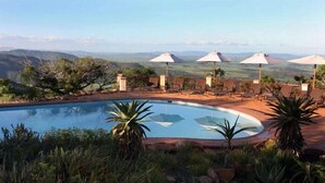 A pool with lounge chairs and umbrellas, surrounded by greenery and hills in the background. - Pakamisa Private Game Reserve (Pongola)