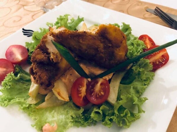 Une assiette contenant un morceau de poulet frit, de la laitue et des tomates cerises.
