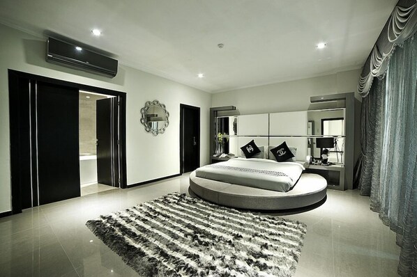 A modern bedroom with a circular bed, a large mirror, and a black and white rug. - New Hotel Nampula (Nampula)