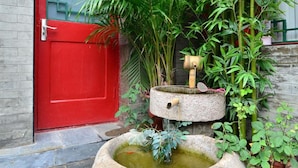 A stone water feature with a bamboo plant and a red door. - Qianmen Courtyard Hotel (Beijing)