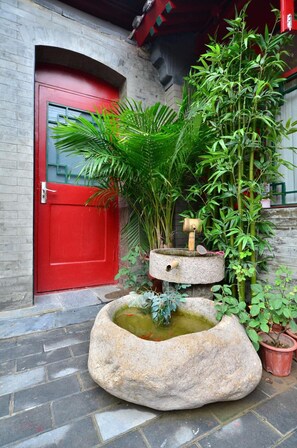 A stone water feature with a bamboo plant and a red door. - Qianmen Courtyard Hotel (Beijing)