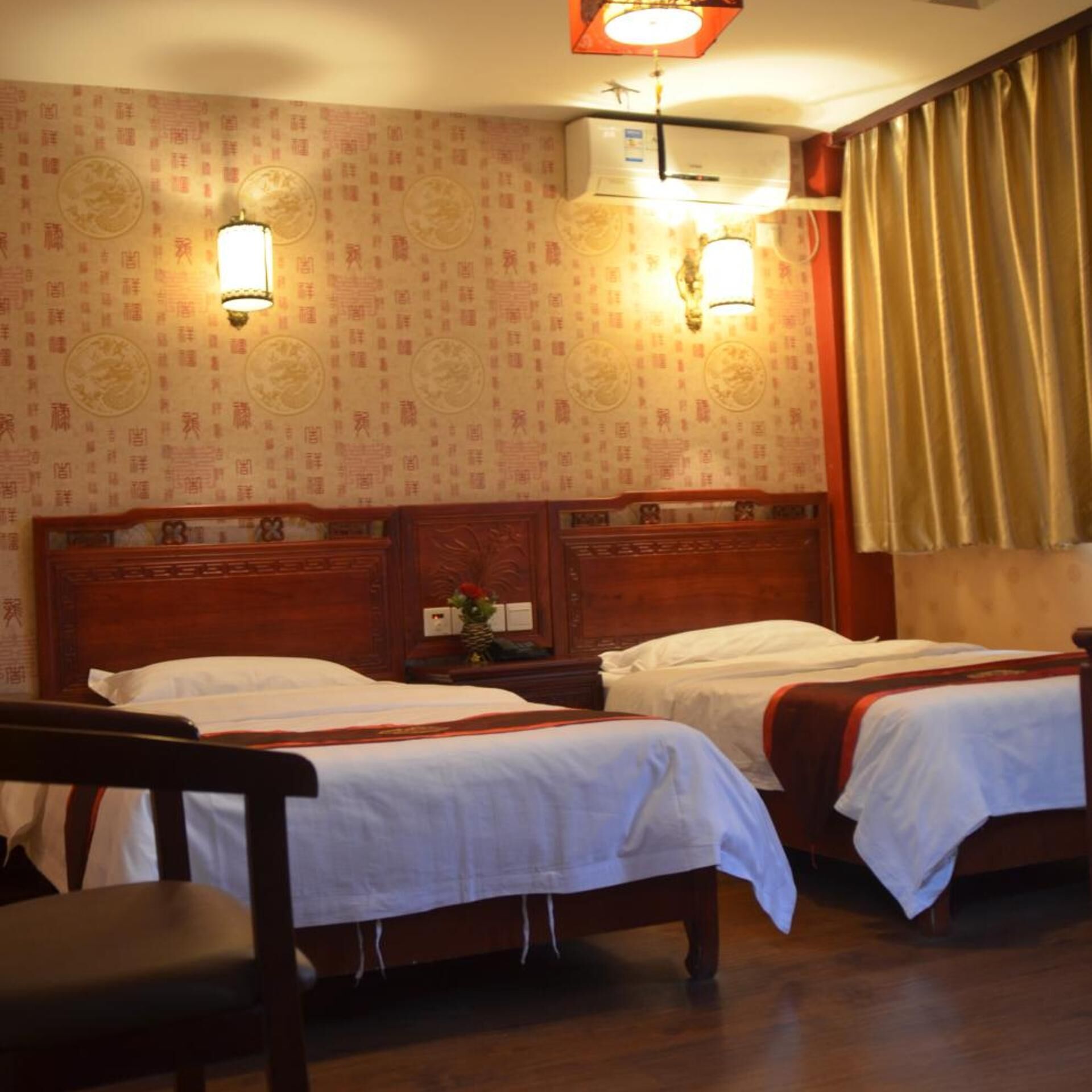 Habitación de hotel con dos camas, cabecera de madera, mesita de noche, una silla y un papel tapiz con diseño.