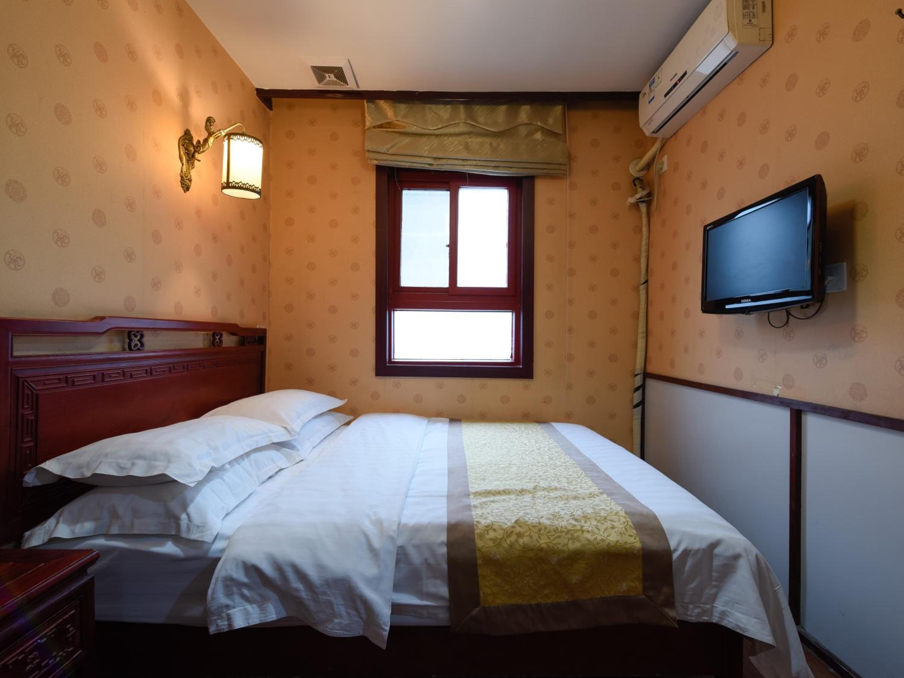 Un dormitorio con una cama, un televisor montado en la pared y una ventana con cortina.