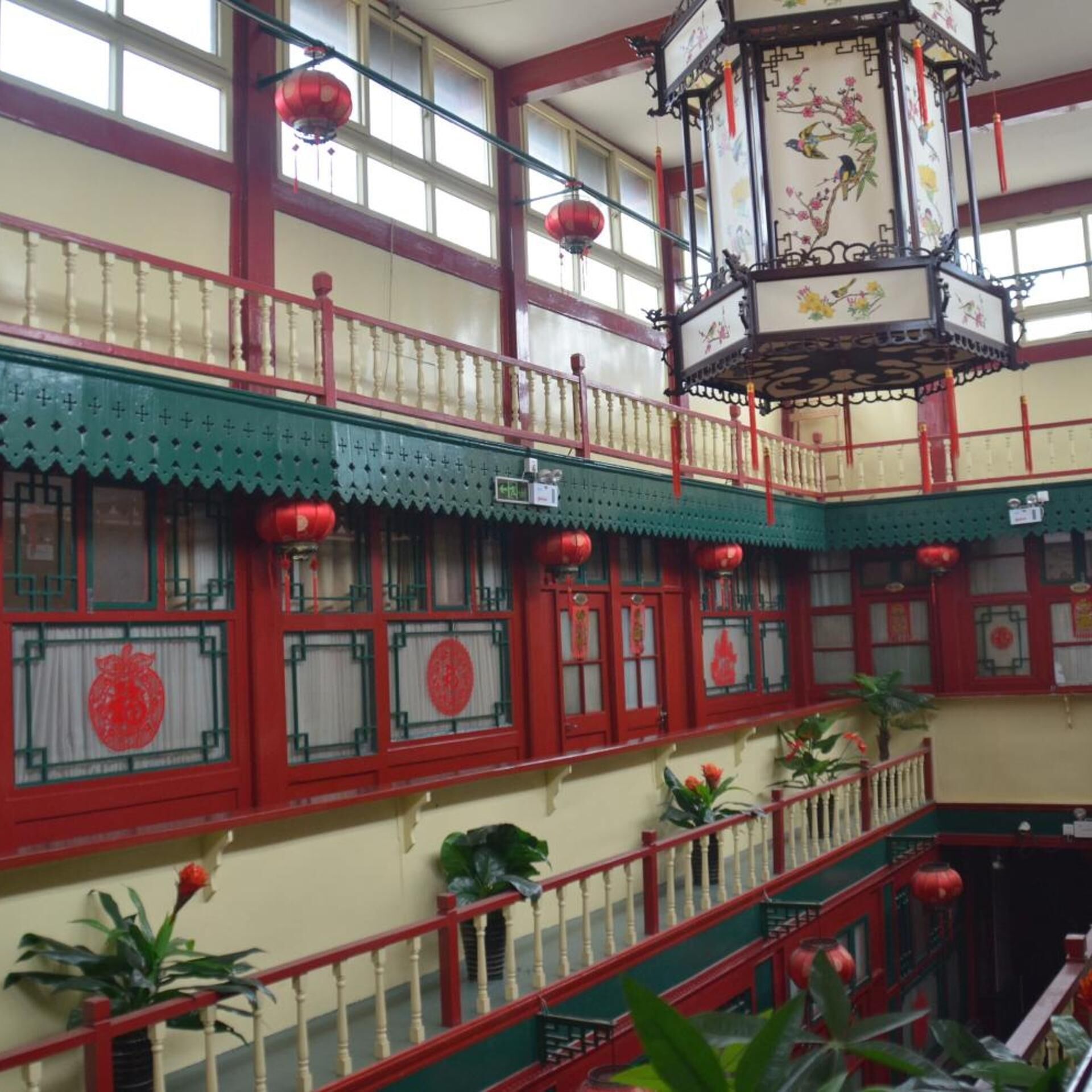 A multi-level building with traditional architectural elements, including red and green color accents, decorative lanterns, and a staircase.