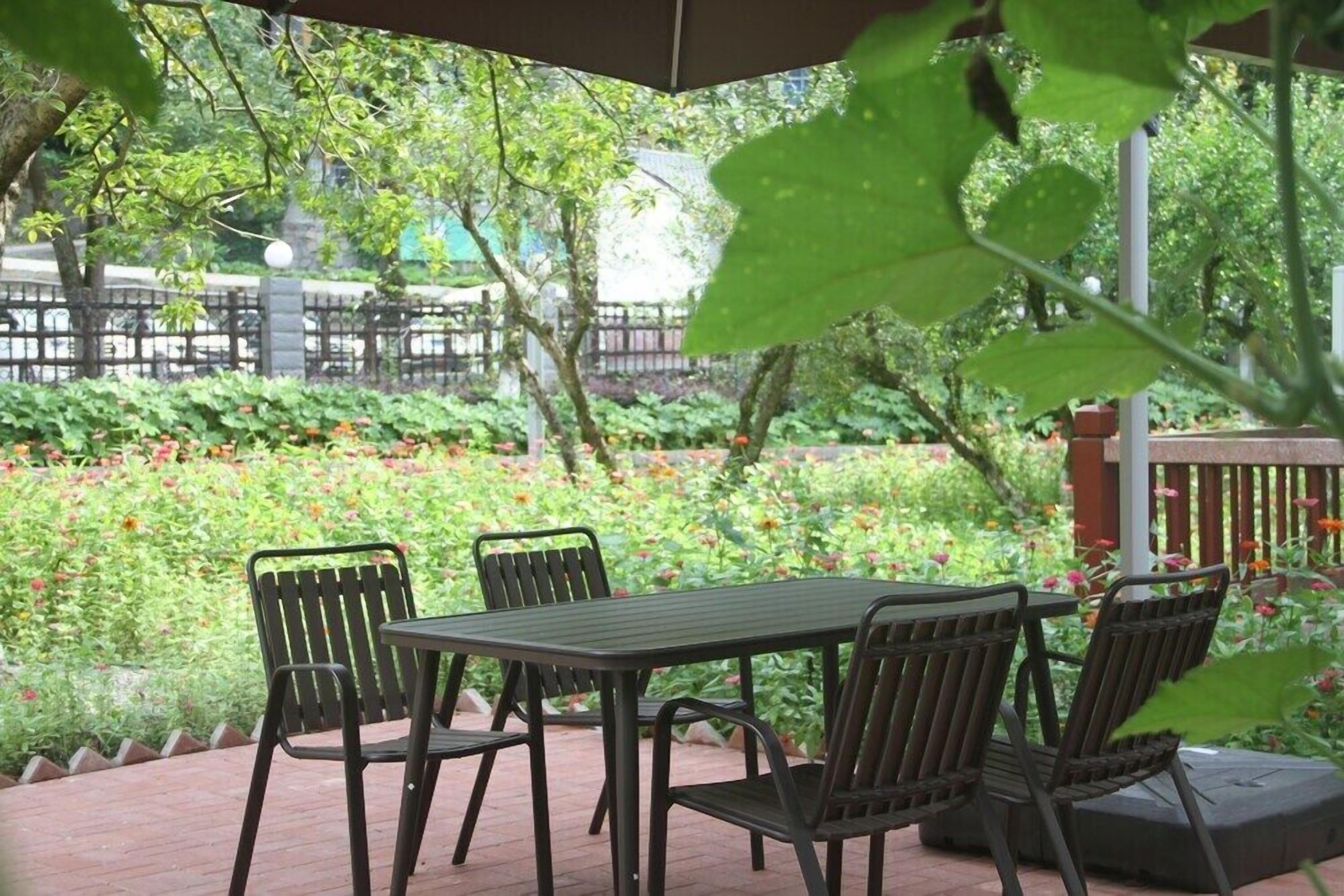 An outdoor patio with a table and chairs, surrounded by lush greenery and flowers.