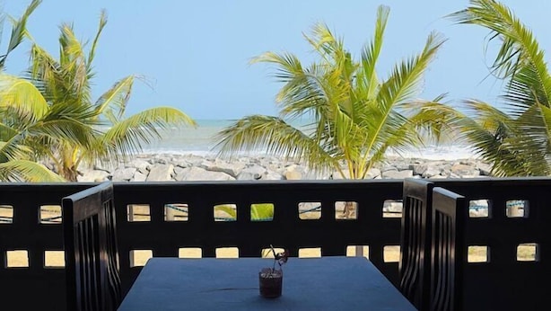 Un tavolo con sedie allestito all'aperto, con vista su una spiaggia di palme e un cielo sereno.