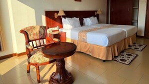 A hotel room with a bed, two bedside lamps, a chair, a small table, and a painting on the wall.