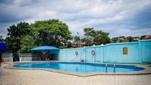 A swimming pool with a tiled deck, surrounded by a low wall and trees.