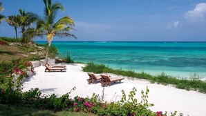 A beach with white sand, two wooden lounge chairs, a palm tree, and clear turquoise water. - Zawadi Hotel Zanzibar (Dongwe)