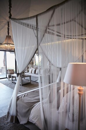 Quarto com cama de dossel, luminária de cabeceira e vista para o exterior.