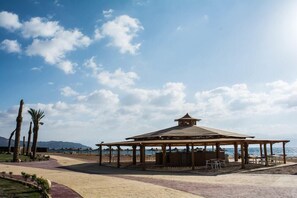 A beachside gazebo with a roof and seating area, surrounded by palm trees and a clear sky. - Tolip Taba Resort And Spa (Taba Heights)