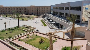 Une cour d’hôtel avec des espaces de détente en plein air, des palmiers et un bâtiment moderne doté de grandes fenêtres.