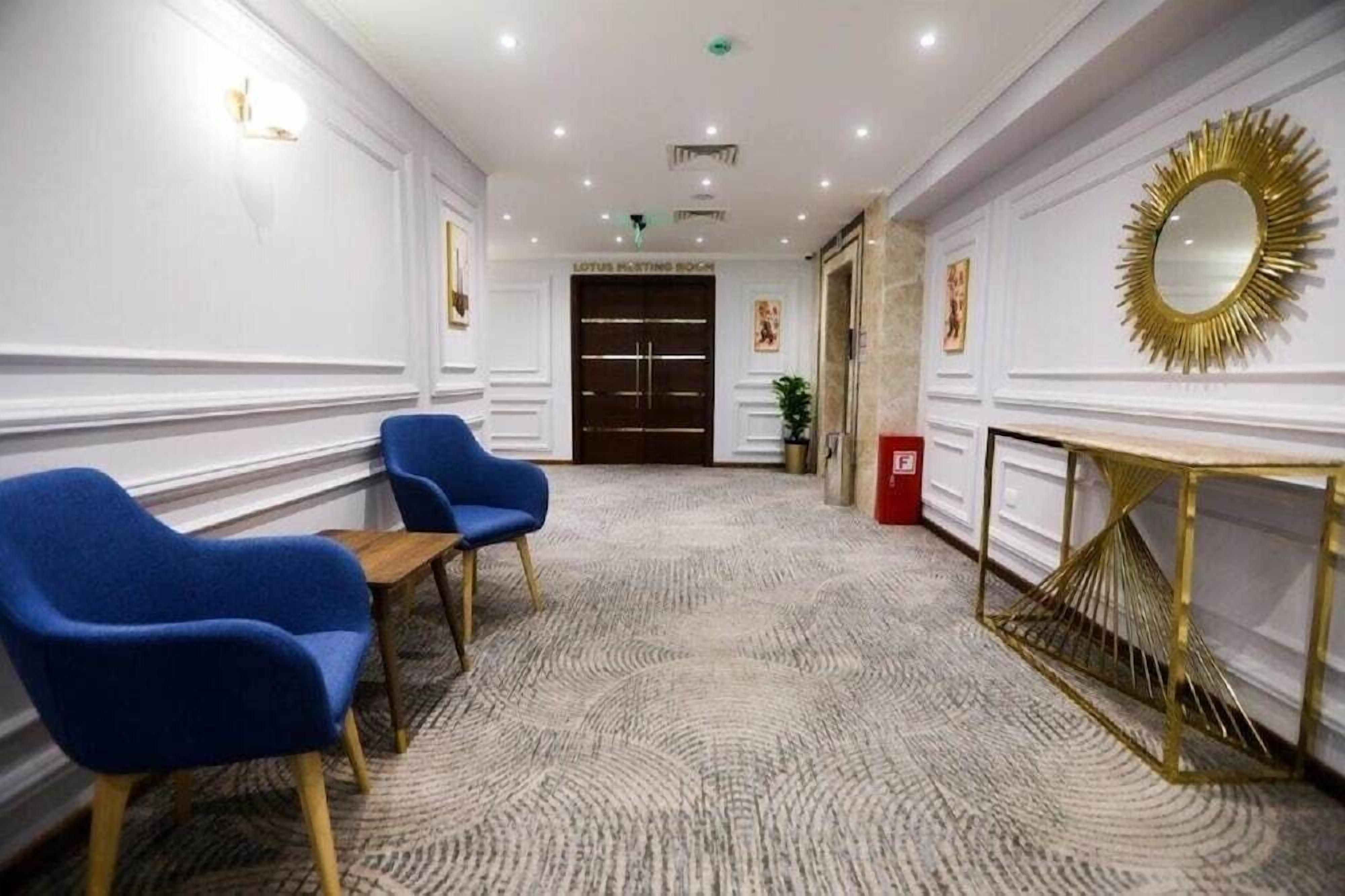 Un hall d’hôtel avec deux fauteuils bleus, une console à cadre doré et un tapis à motifs.
