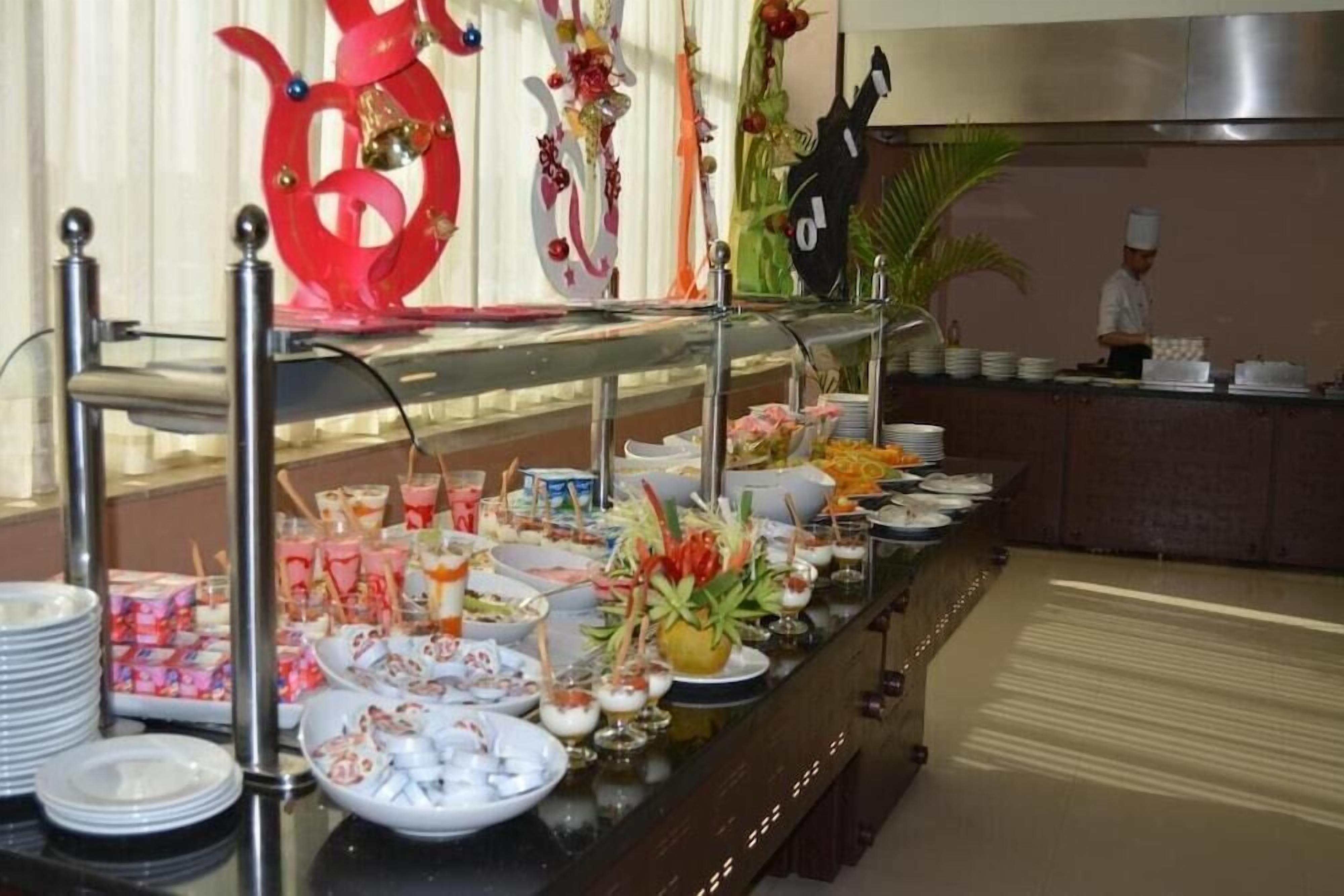 Ein reichhaltiges Buffet mit verschiedenen Speisen und Getränken, im Hintergrund ein Koch sowie dekorative Elemente an der Wand.