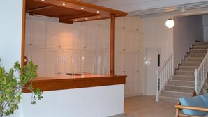 A modern interior with a wooden reception desk, white cabinets, a staircase, and two wooden chairs. - Faros (Spetses)