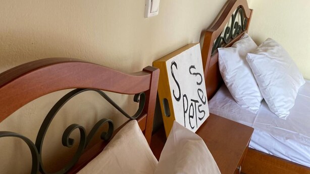 A bedroom with a bed, pillows, a sign, and a wall switch. - Faros (Spetses)