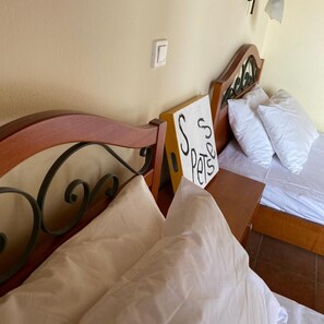A bedroom with a bed, pillows, a sign, and a wall switch. - Faros (Spetses)