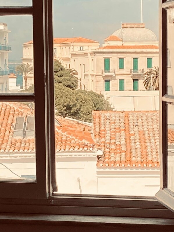 Blick durch ein Fenster auf ein Gebäude mit einem Ziegeldach und einen großen Baum im Vordergrund.